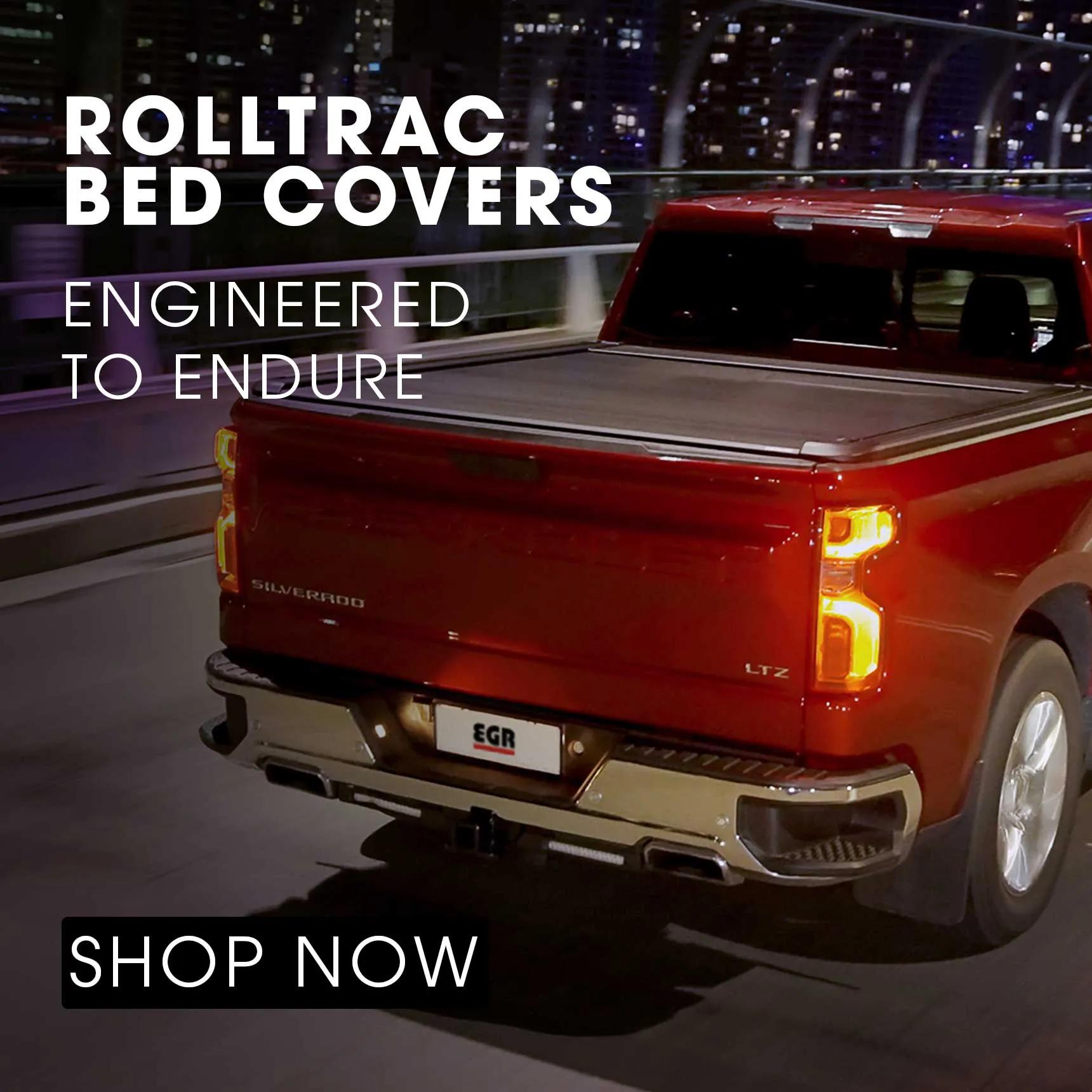 Red Chevrolet Silverado driving over a city bridge at night with a closed EGR RollTrac retractable bed cover