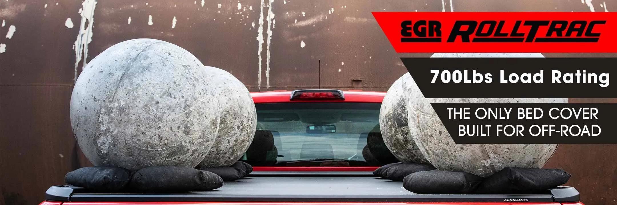 EGR RollTrac hard bed cover on a red pickup truck supporting two large concrete balls, demonstrating its 700 lb load rating